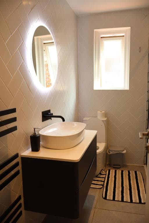 Bathroom with a basin on a vanity unit and a lit round mirror